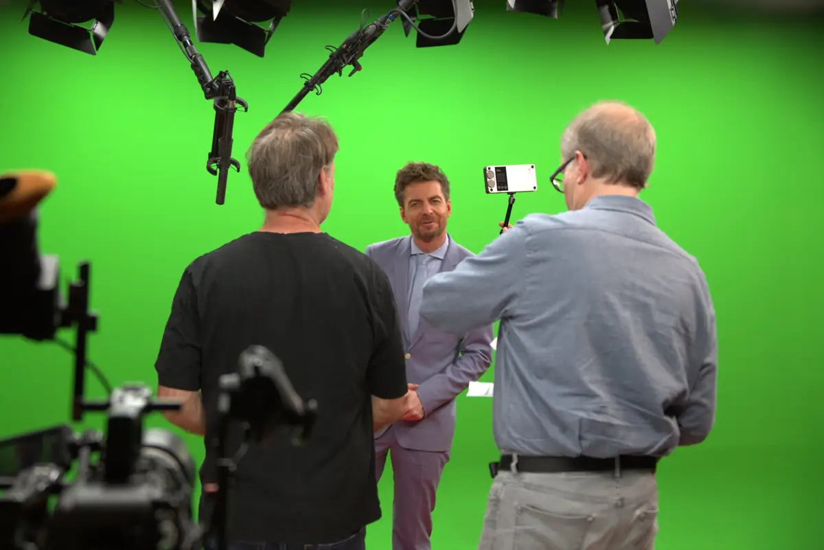 Interview-Dreh im Greenscreen Studio München: Moderator vor grüner Hohlkehle mit Kamerateam, Boom-Mikrofonen und Fresnel-Scheinwerfern – LANIZMEDIA GmbH