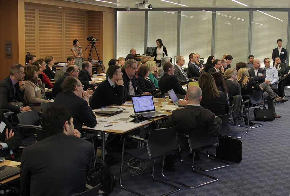 Konferenz-Mitschnitt im Tagungsraum mit Kamera auf Stativ und Teilnehmern an Tischen