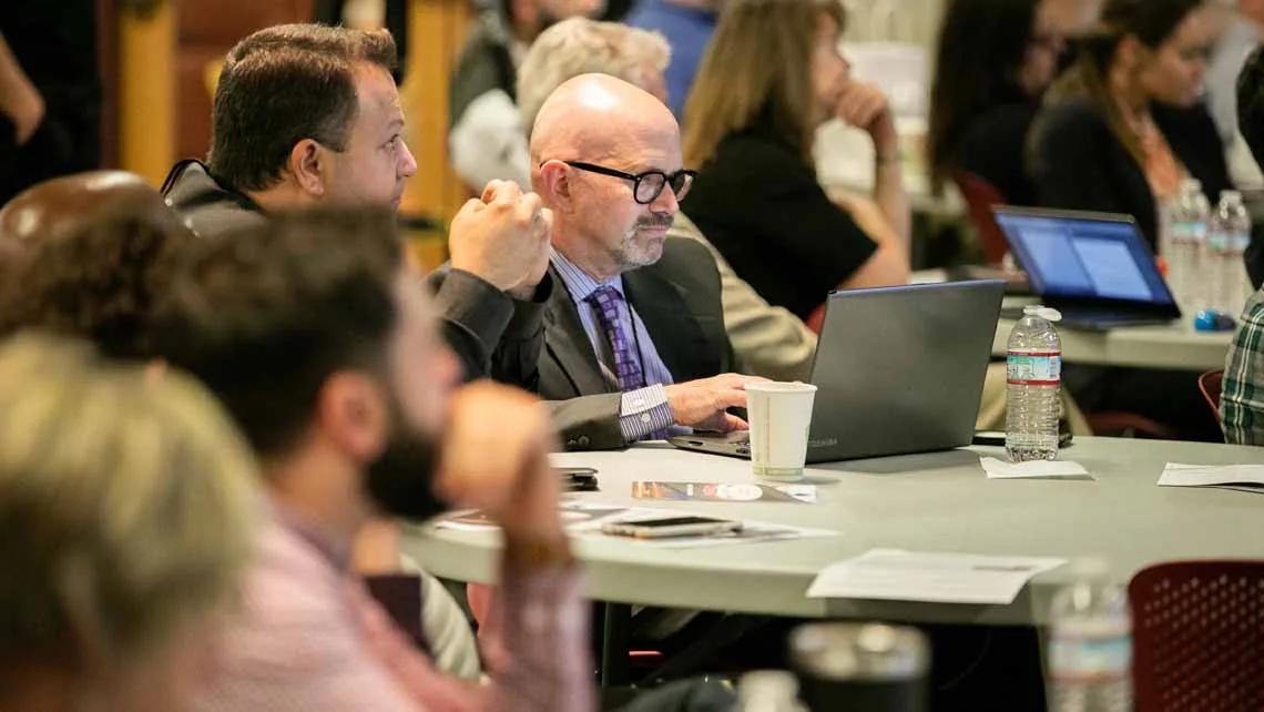 Workshop-Teilnehmer mit Laptops an runden Tischen während einer Tagung